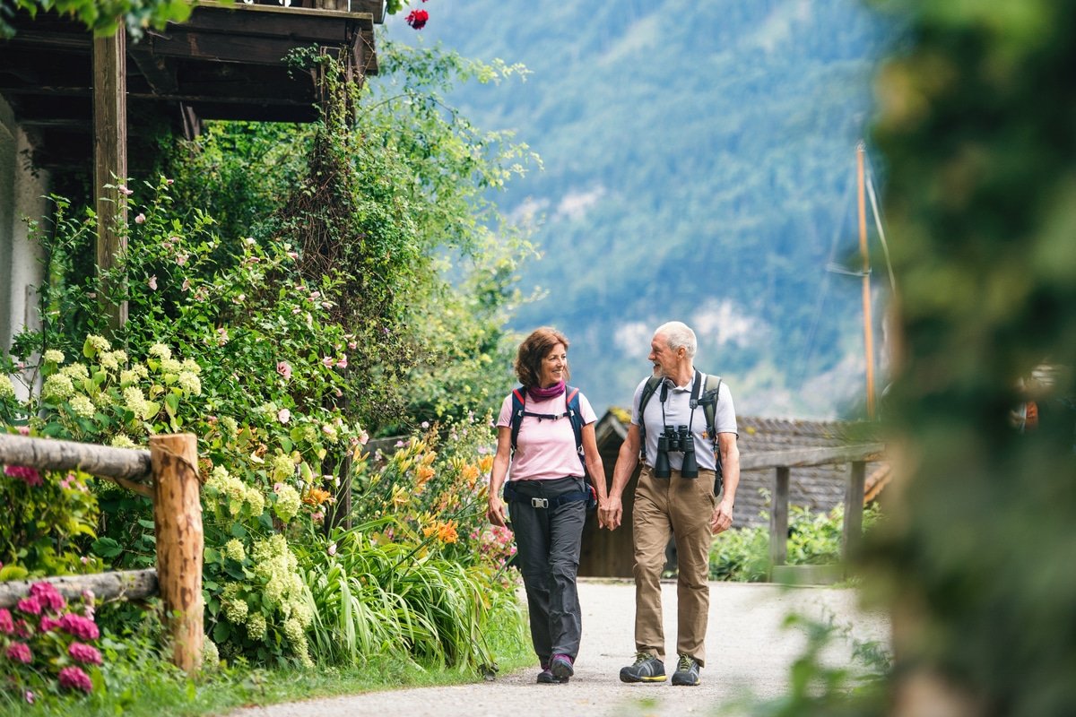 a senior pensioner couple with binoculars hiking, holding hands.